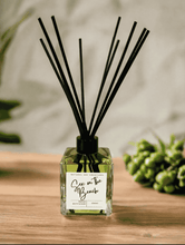 Load image into Gallery viewer, Sex on the Beach reed diffuser by Natural Soy Creations, displayed on wooden surface with black reeds and green foliage in background.