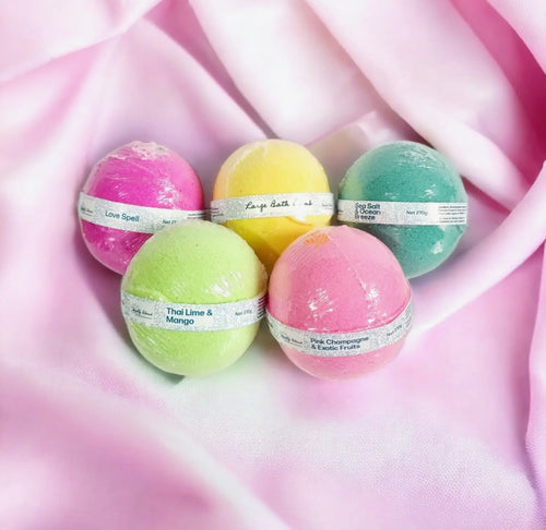 Assorted large bath bombs by Natural Soy Creations in vibrant colours displayed on soft pink fabric background.