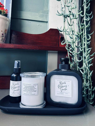 Bathroom gift set featuring a medium Monaco candle, room spray, and goats milk hand soap arranged neatly on a black tray beside indoor greenery.