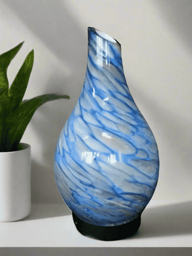 Blue ultrasonic diffuser with elegant glass design, displayed on a white shelf beside a potted plant.