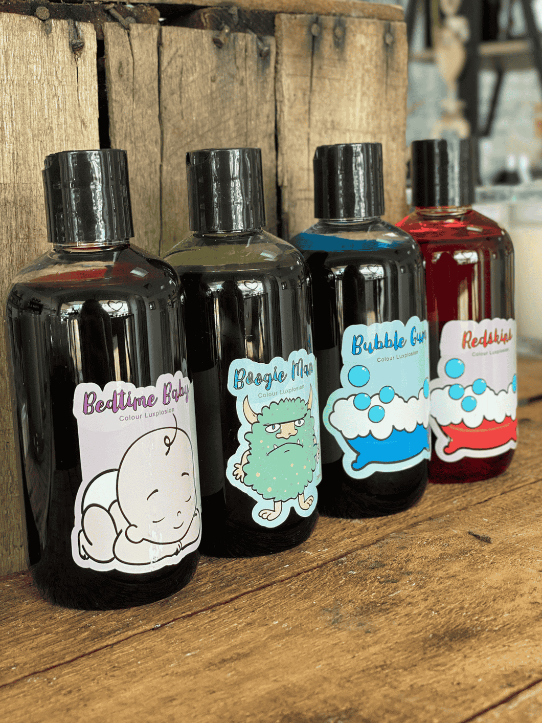 Colourful bottles of handmade bubble bath displayed on wooden surface, vibrant bath additives by A Lil Luxury.