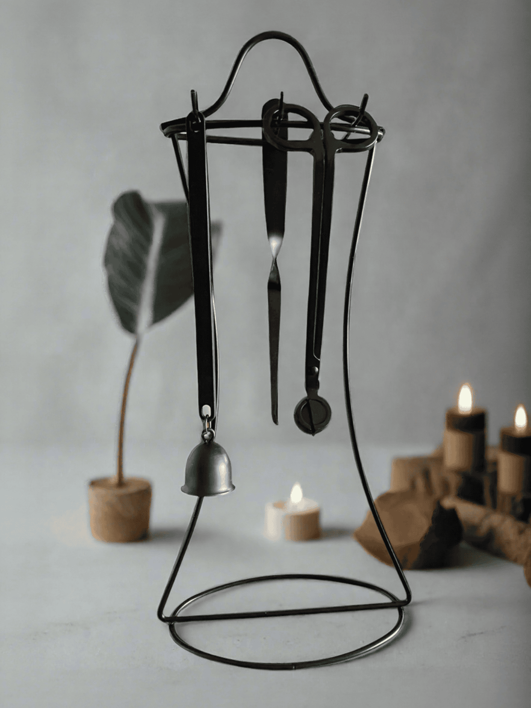 Candle care kit with wick trimmer, snuffer, and dipper tools displayed on a black metal stand.