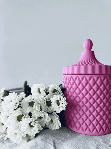 Deluxe matt pink geo soy candle in a textured glass jar with lid, styled beside fresh white flowers.