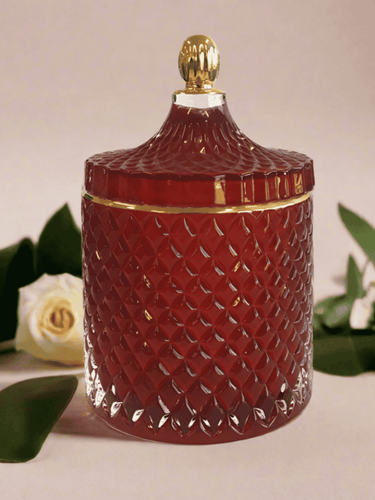Deluxe royal red geo soy candle with gold trim lid, displayed with white roses and green foliage for an elegant look.