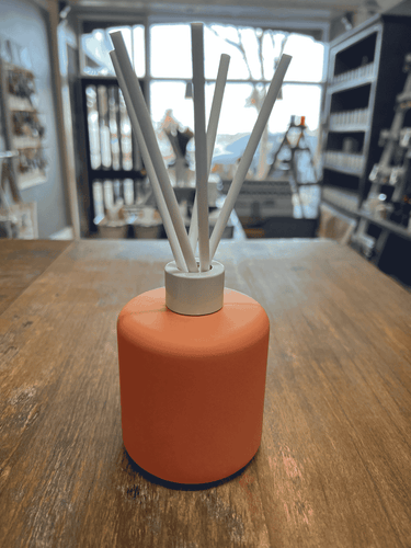 Orange matte reed diffuser with white reeds for fresh fragrance.