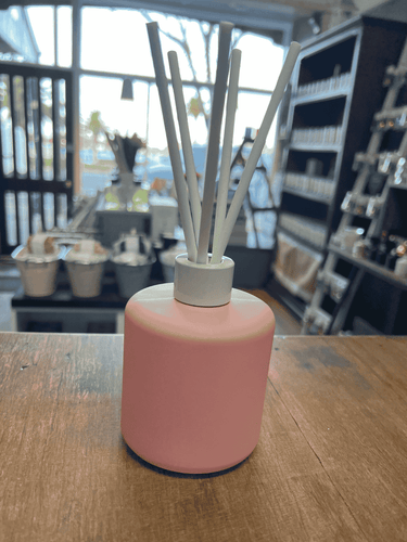 Pink matte reed diffuser with white reeds on wooden surface.