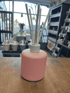 Pink matte reed diffuser with white reeds on wooden surface.