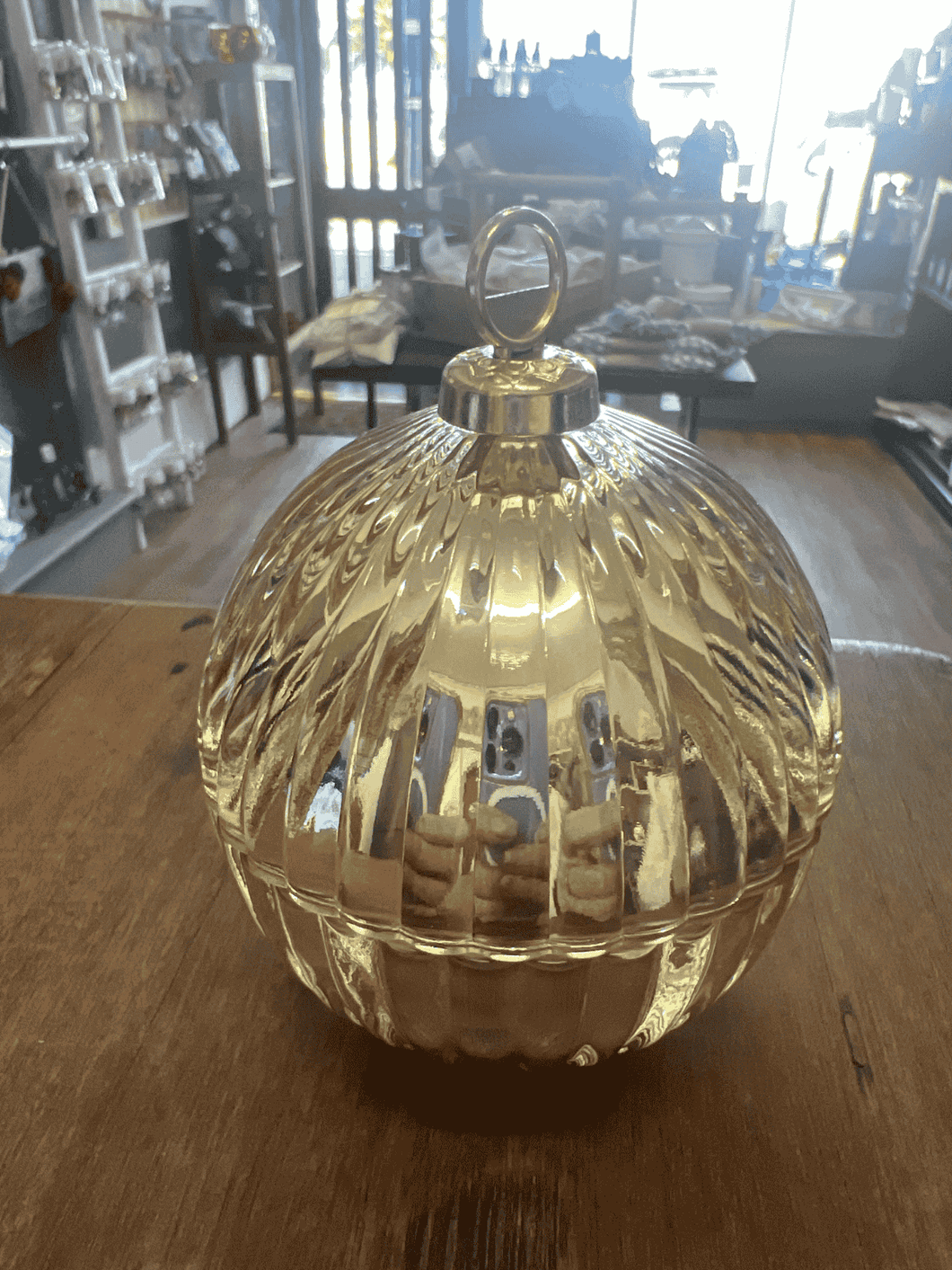 Close-up of a gold mini bauble candle on a wooden surface, reflecting warm ambient light.
