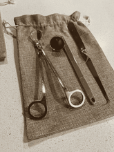 Load image into Gallery viewer, Gold candle care kit with wick trimmer, snuffer, and dipper neatly arranged on a hessian storage bag.
