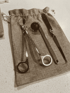 Gold candle care kit with wick trimmer, snuffer, and dipper neatly arranged on a hessian storage bag.