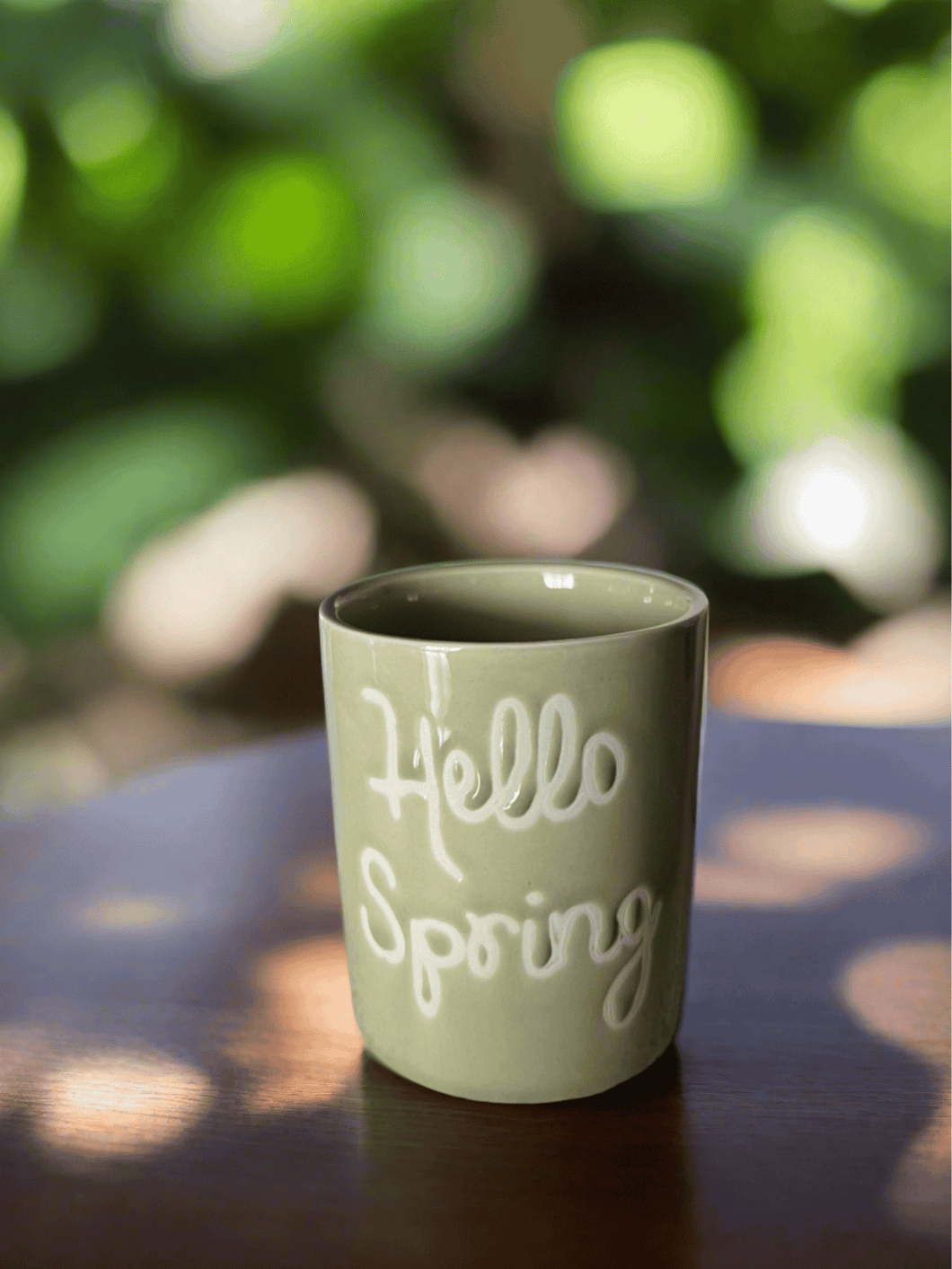 Natural Soy Creations Hello Spring soy candle in a green glass jar with white lettering, displayed outdoors.