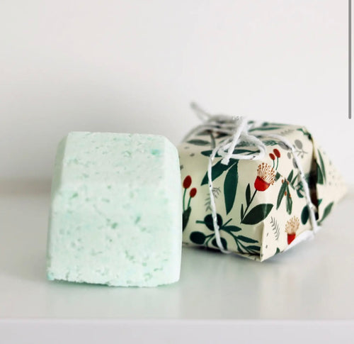 Natural Soy Creations Lemon Myrtle and Niaouli bath bomb in pale green, displayed with floral wrapping on white surface.
