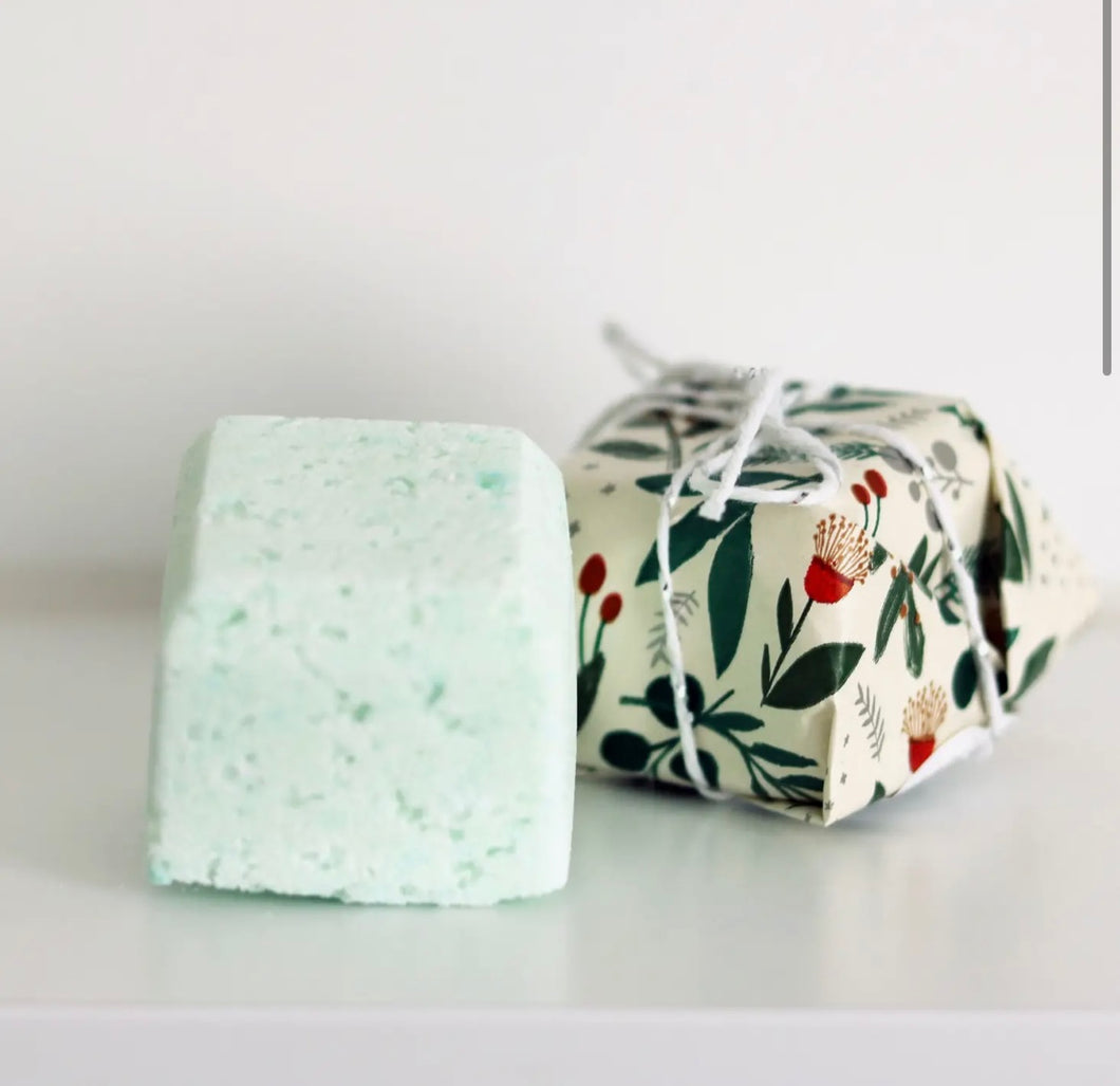 Natural Soy Creations Lemon Myrtle and Niaouli bath bomb in pale green, displayed with floral wrapping on white surface.