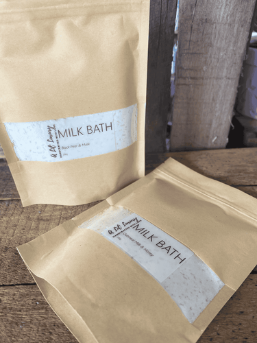 Two kraft pouches of natural coconut milk bath powder displayed on wooden surface, soothing and hydrating bath soak.