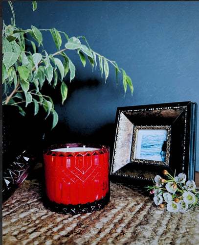 Red mandala glass soy candle with textured geometric design, styled on a woven surface beside a photo frame and flowers