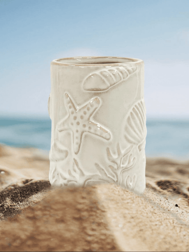 Seaside soy candle by Natural Soy Creations displayed on sand with ocean backdrop, coastal-inspired candle jar.
