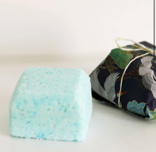 Natural Soy Creations Sleep Tight bath bomb in light blue, shown with dark floral wrapping on white surface.
