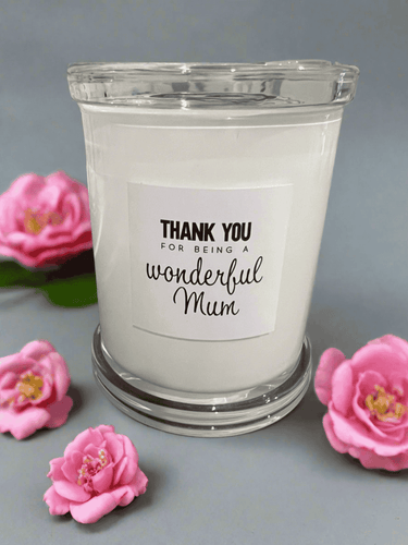 White glass candle with the message: Thank you for being a wonderful Mum, styled with pink flowers.