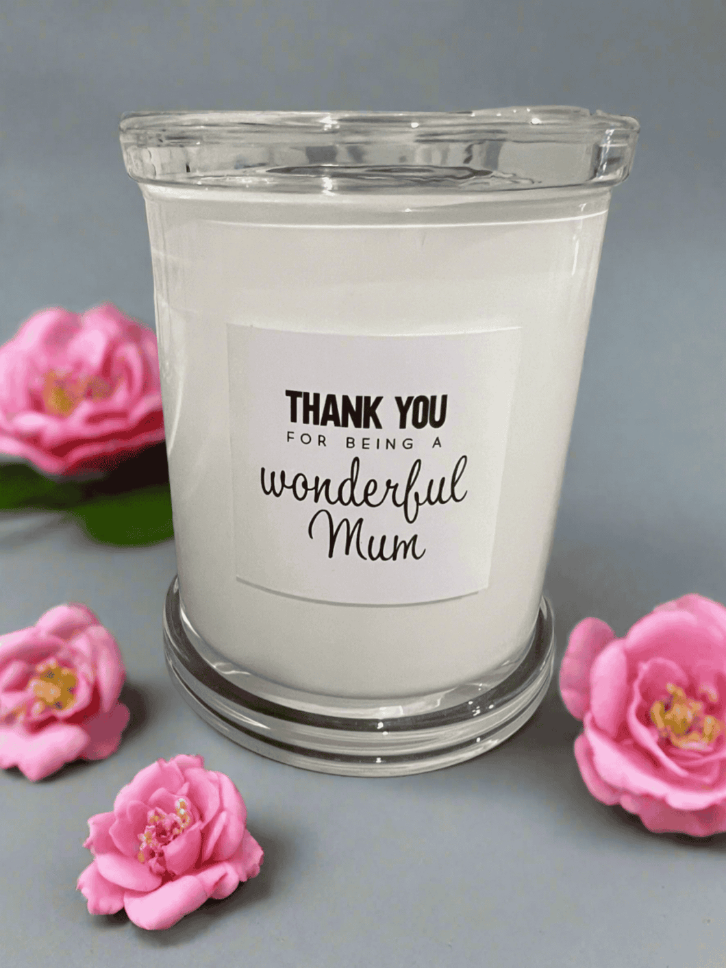 White glass candle with the message: Thank you for being a wonderful Mum, styled with pink flowers.