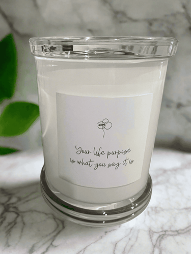 White glass candle with the inspirational message: Your life purpose is what you say it is, featuring a simple flower line illustration.